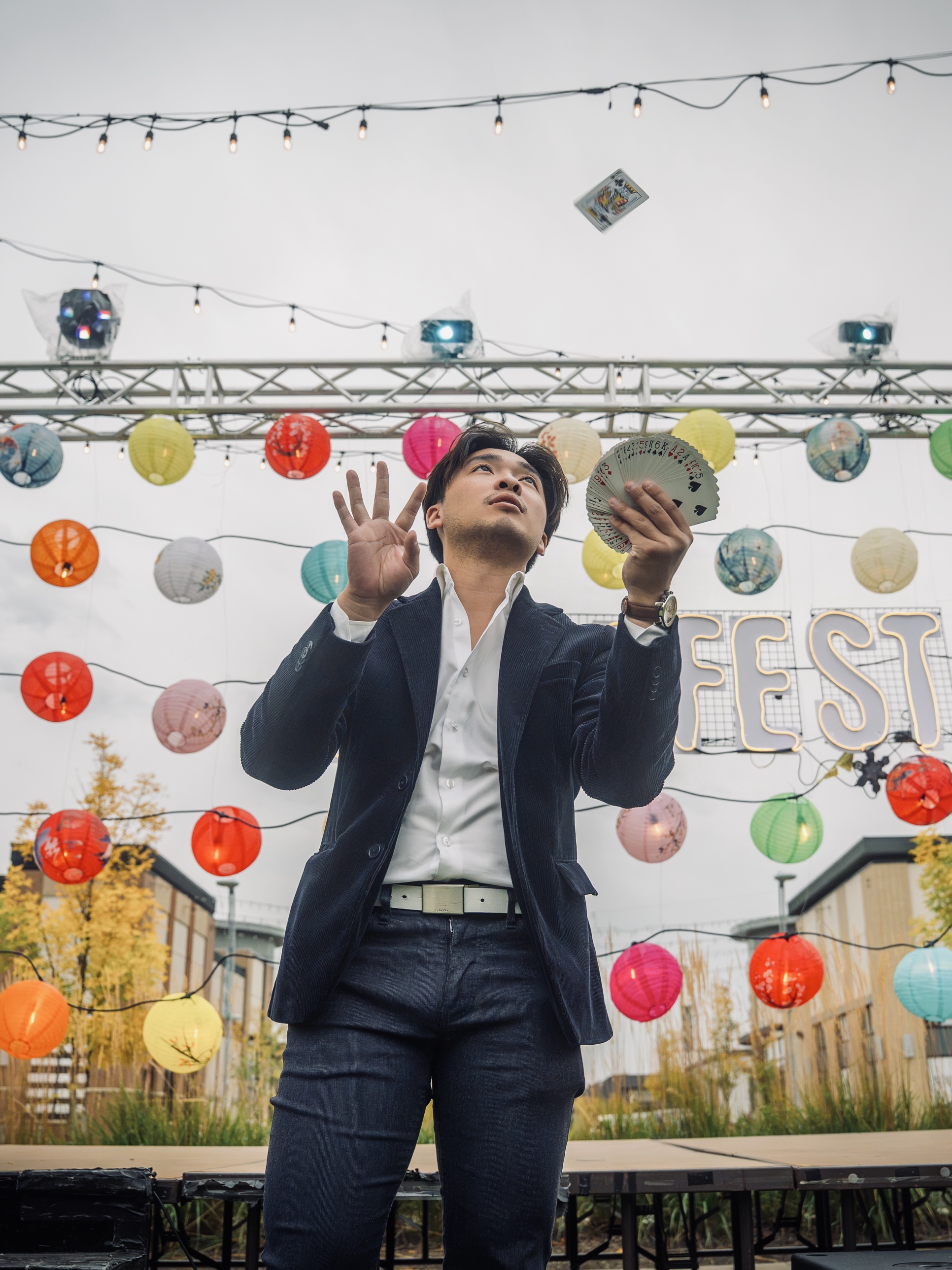 Jason Wong tossing a playing card into the air on an outdoor festival stage strung with lanterns